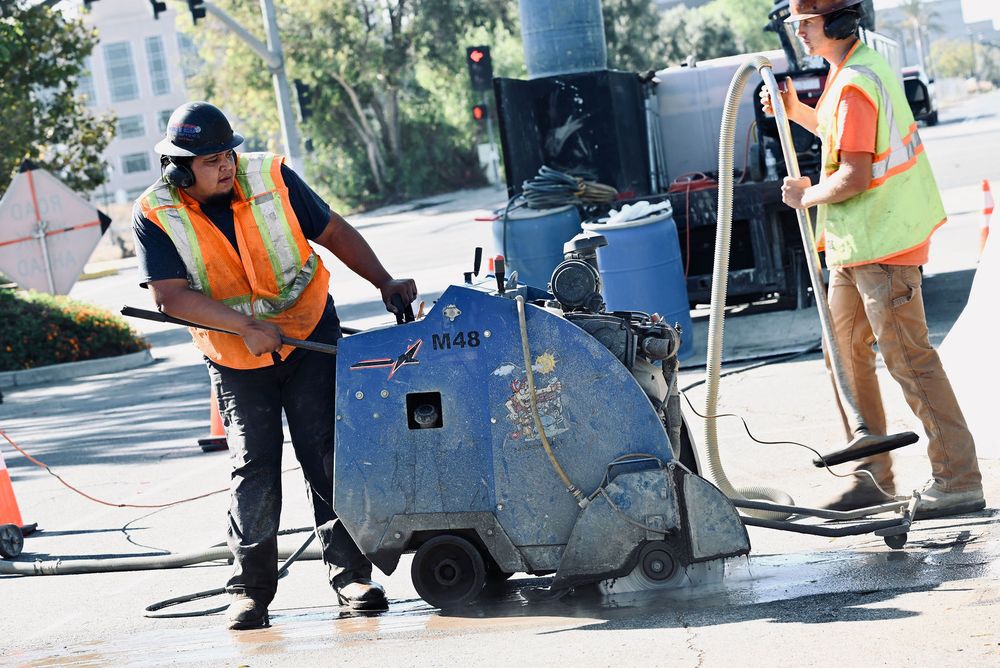 Two crew members wet-cutting pavement with a walk-behind flat saw