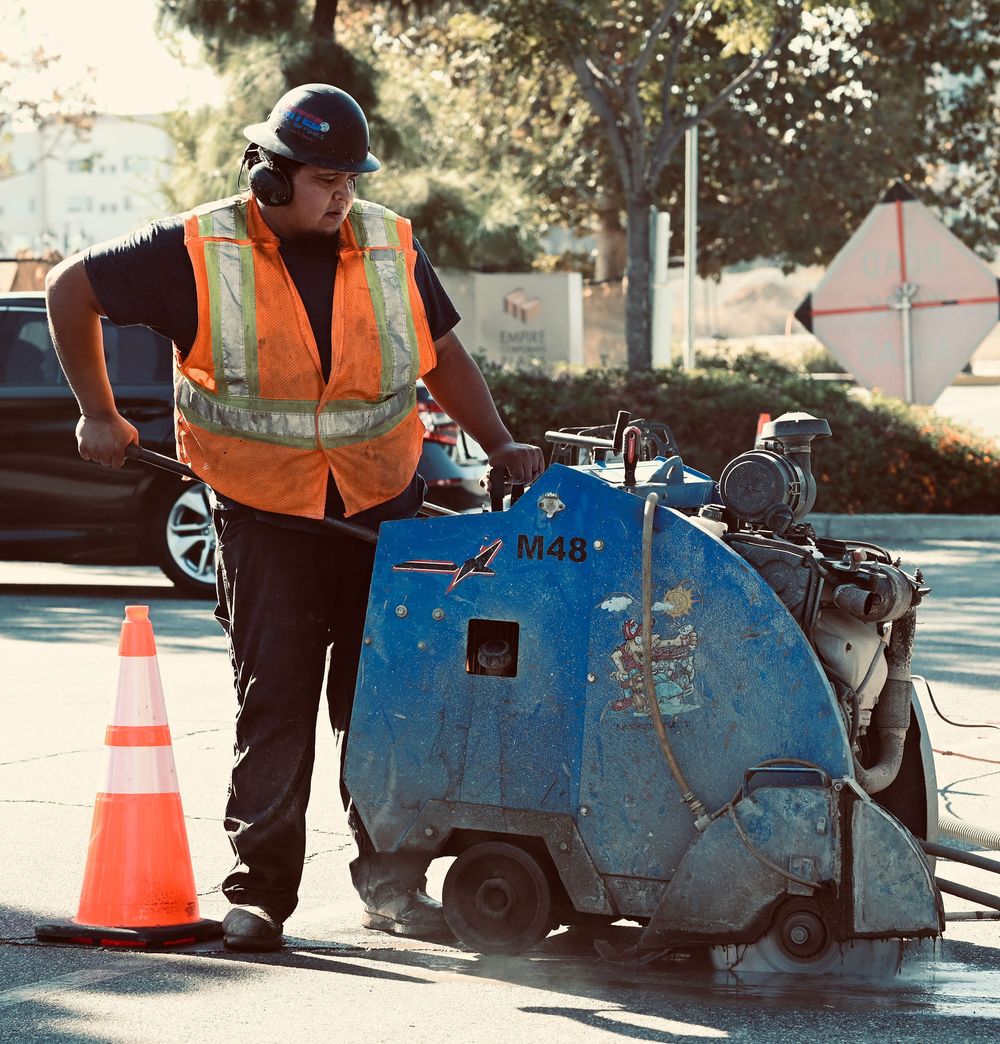 Operator flat-sawing wet pavement beside a traffic cone