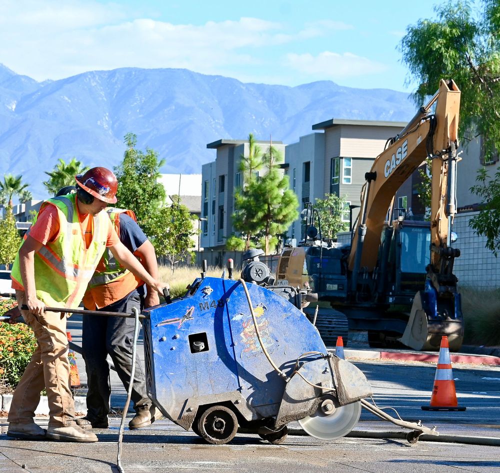 Two operators flat-sawing a street in front of an excavator